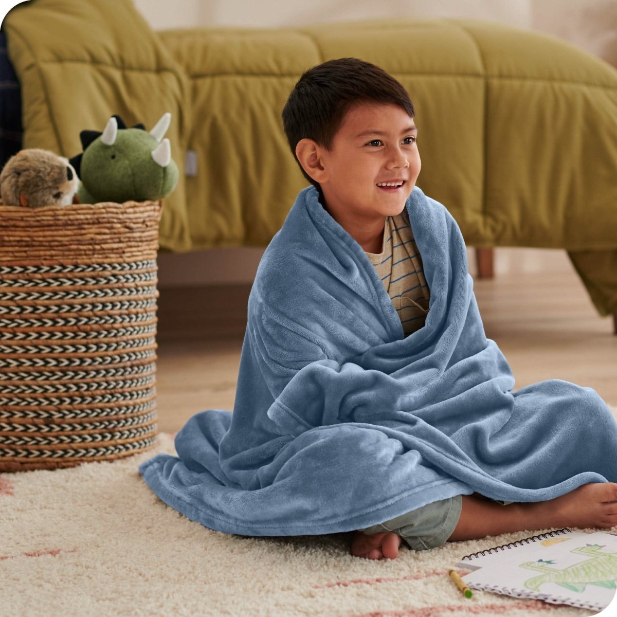A boy is sitting on the floor of his bedroom with a microplush blanket wrapped around him