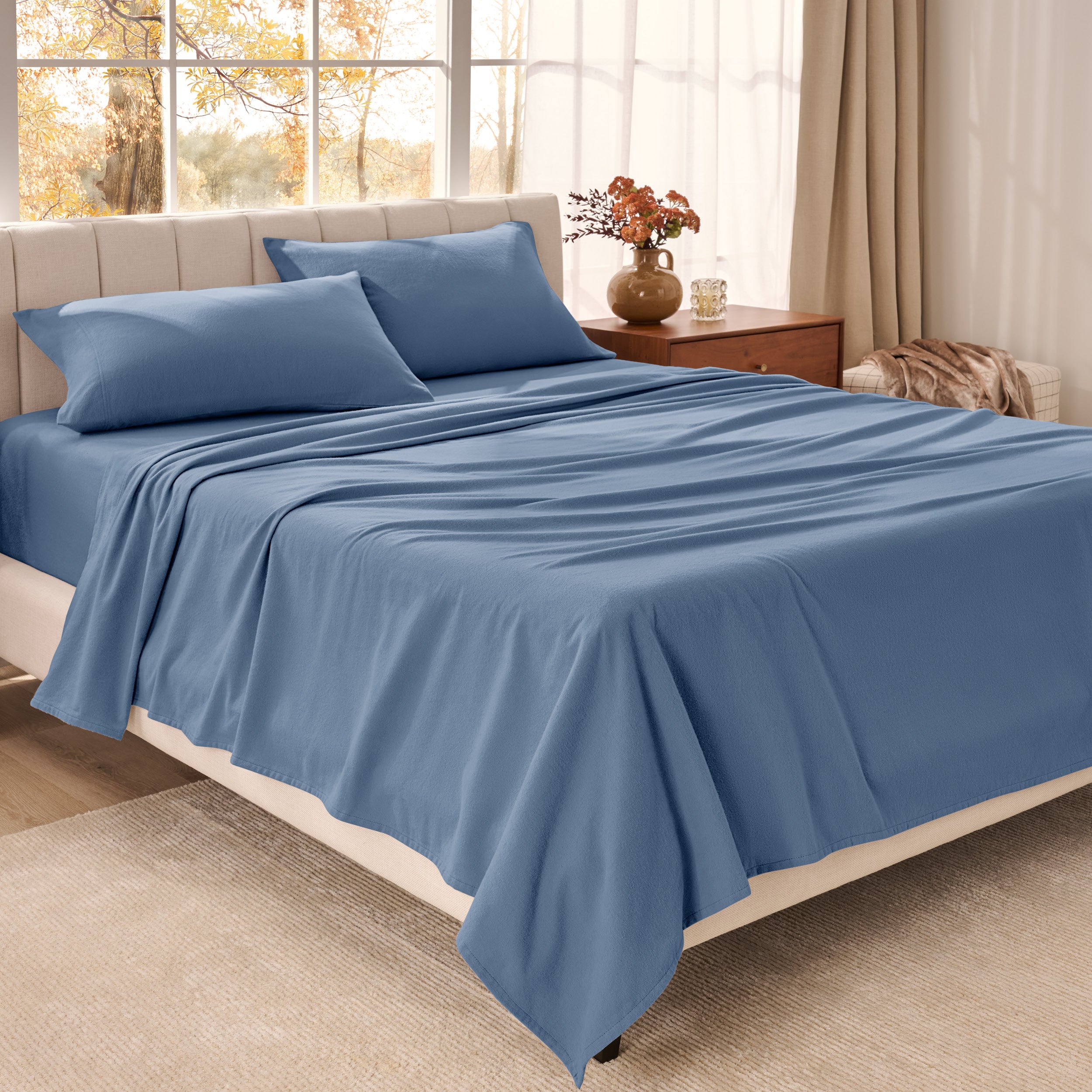Bed sheets on a neatly made bed in a bright bedroom with large windows.