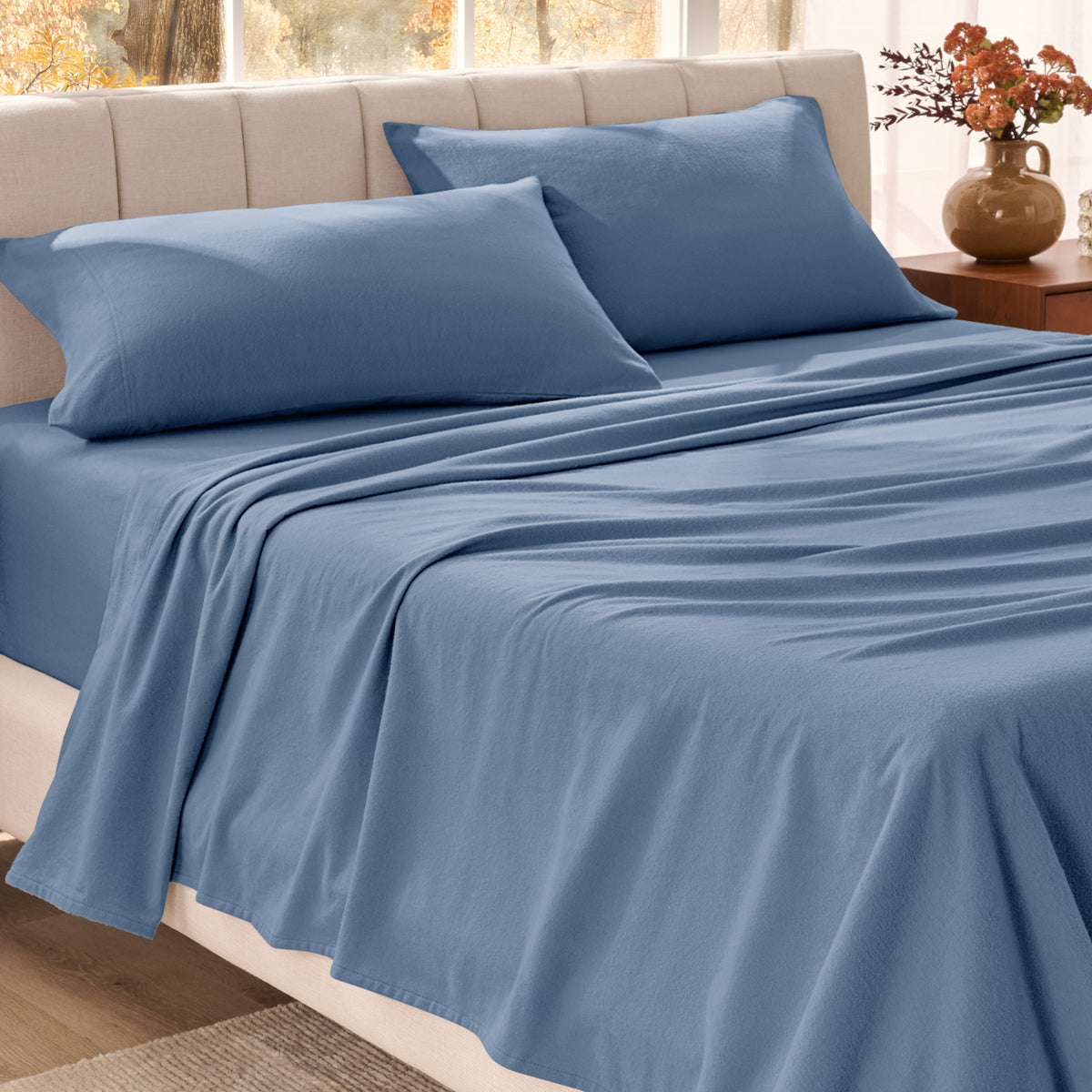 Bed sheets on a neatly made bed in a bright bedroom with large windows.