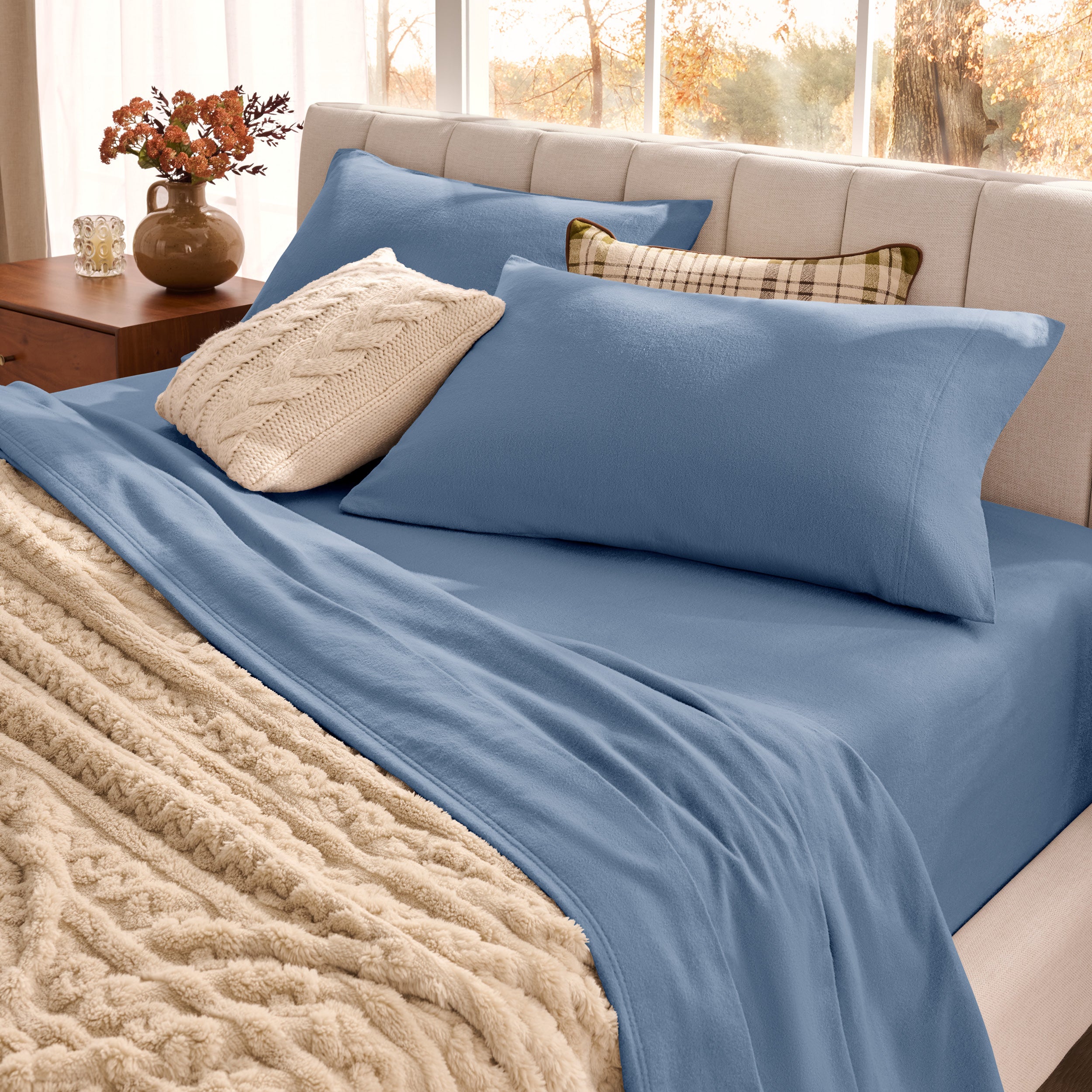 Neatly made bed with organic flannel sheets  and a beige blanket in a bright bedroom.