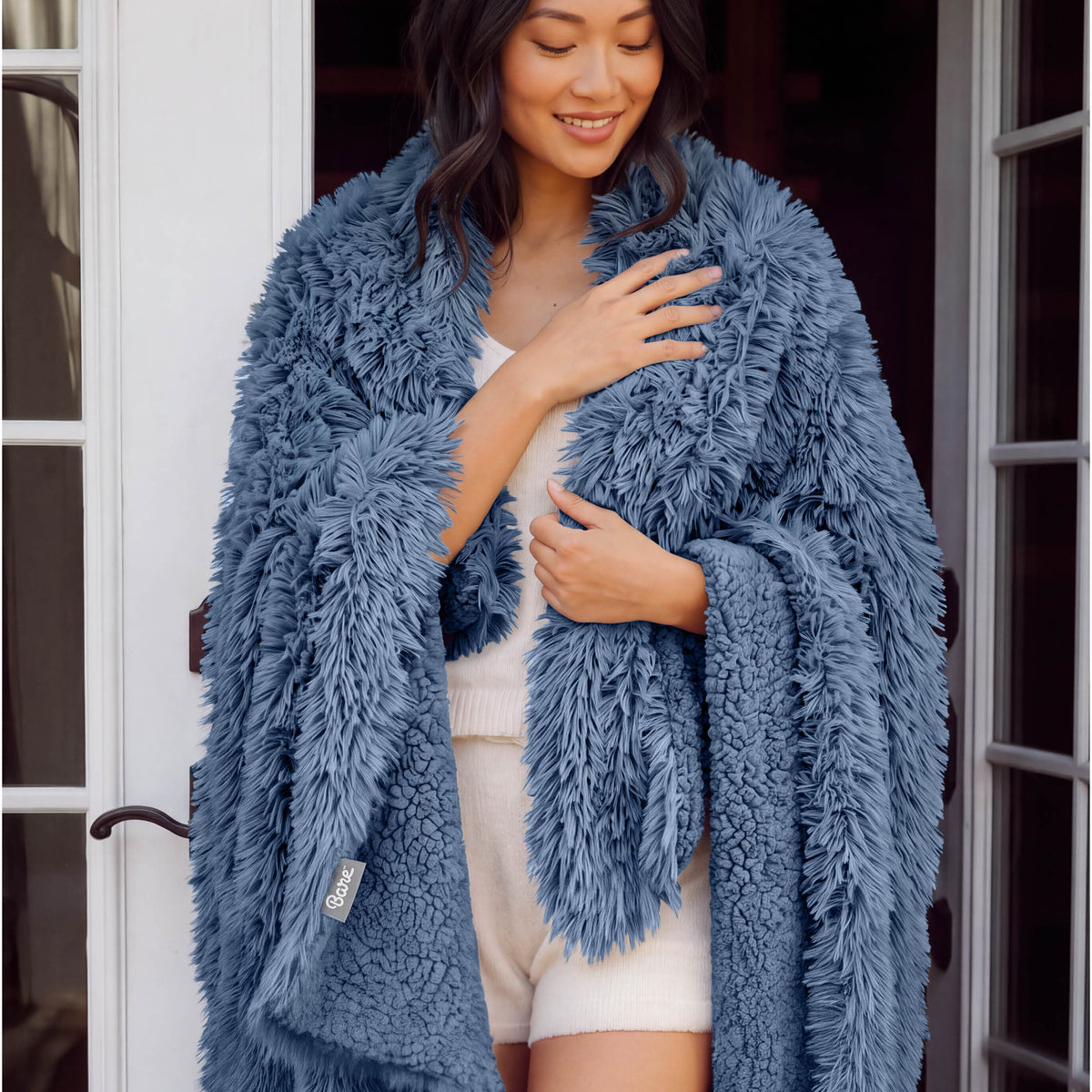 A woman standing with a shaggy blanket wrapped around her