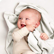 A baby lying on a receiving blanket. She has her thumb in her mouth.