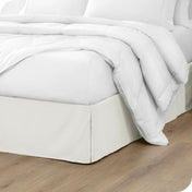 A modern bed with a microfiber bed skirt with pleats on the corners and midway on each side.