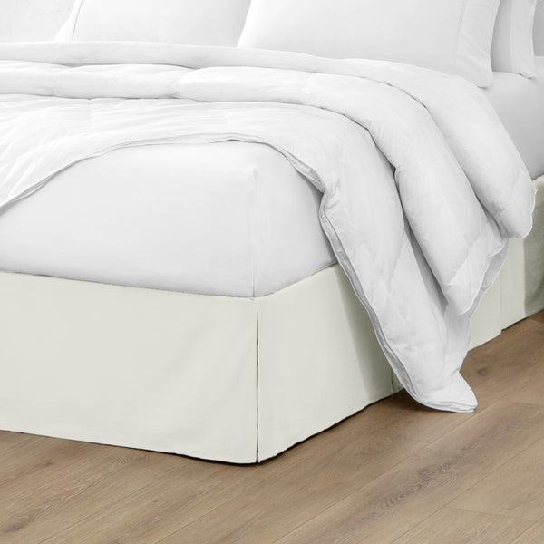 A modern bed with a microfiber bed skirt with pleats on the corners and midway on each side