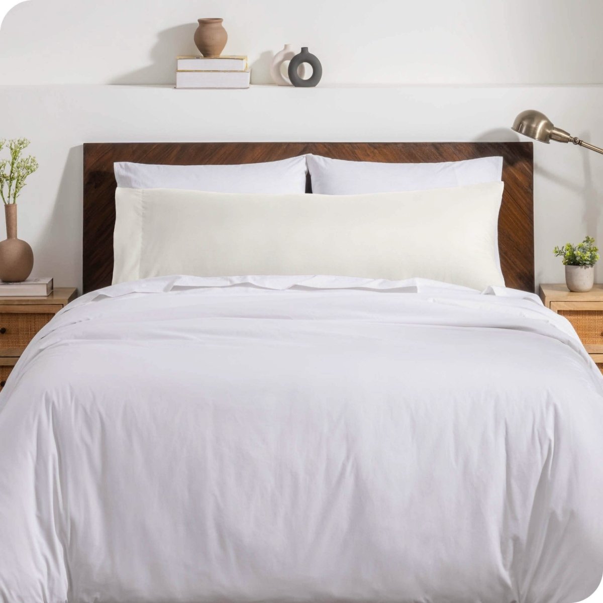 A body pillow cover on a pillow on a bed with other pillows and a duvet cover