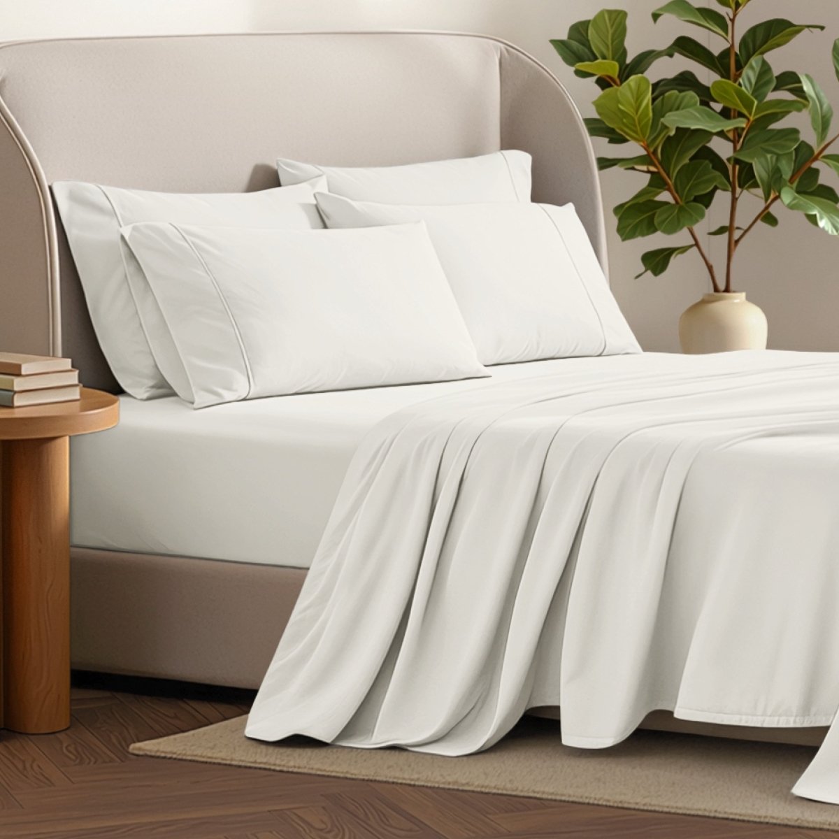 Bed sheets and pillows on a bed with a plant and side table in the background.