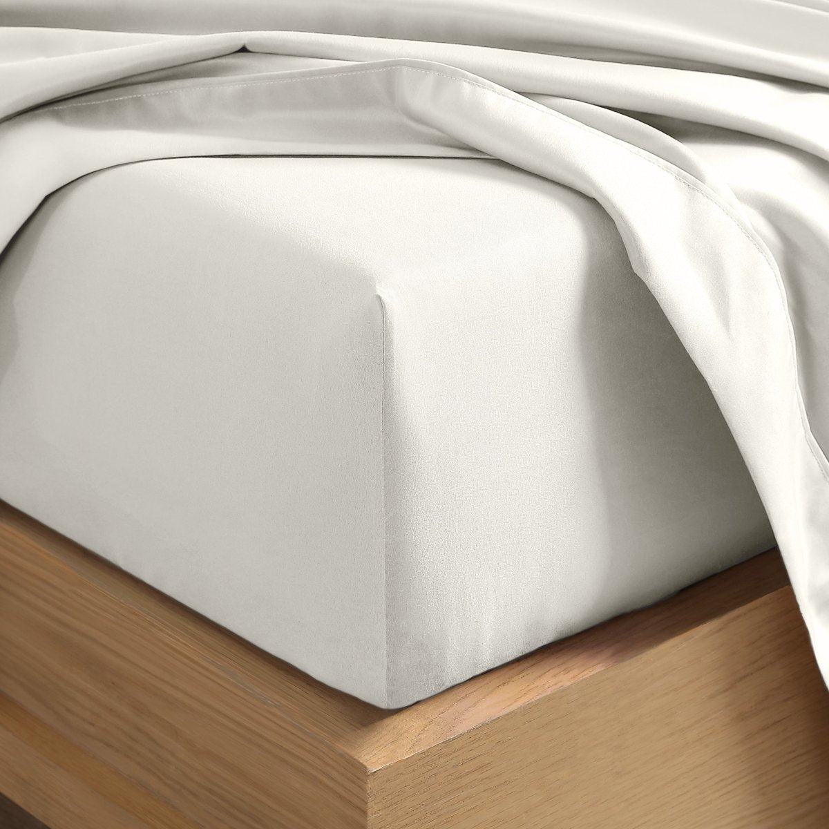 A close-up of a fitted sheet covering the corner of a bed frame, with matching top sheet draped over it.