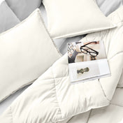 Close up of a comforter set on a bed. There are glasses and a magazine on top of the comforter.