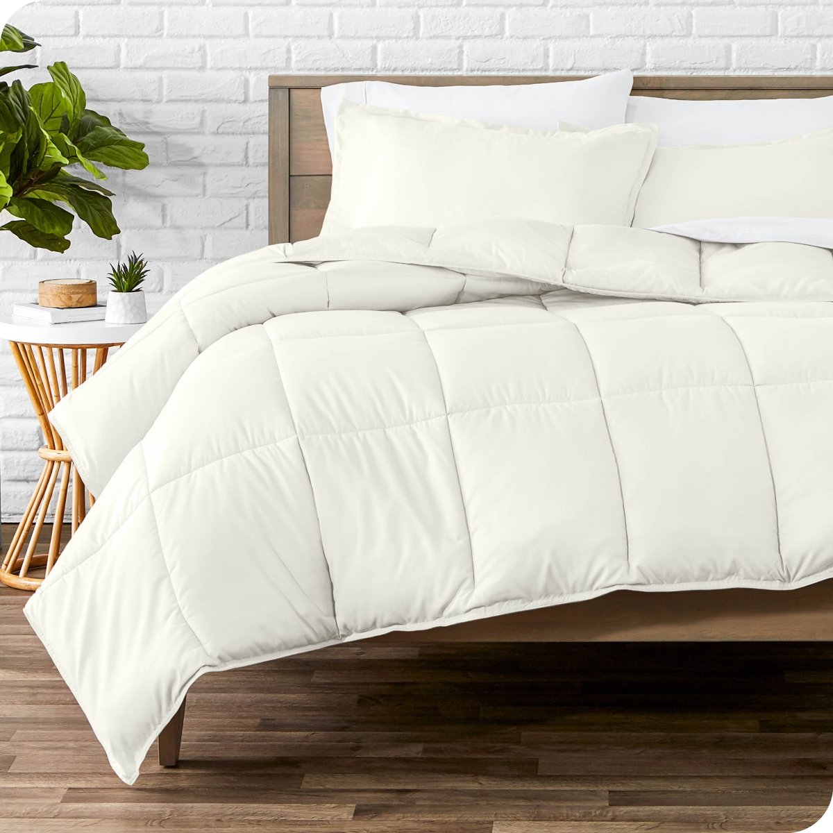 Comforter set on a bed with a white brick wall and plant in the background