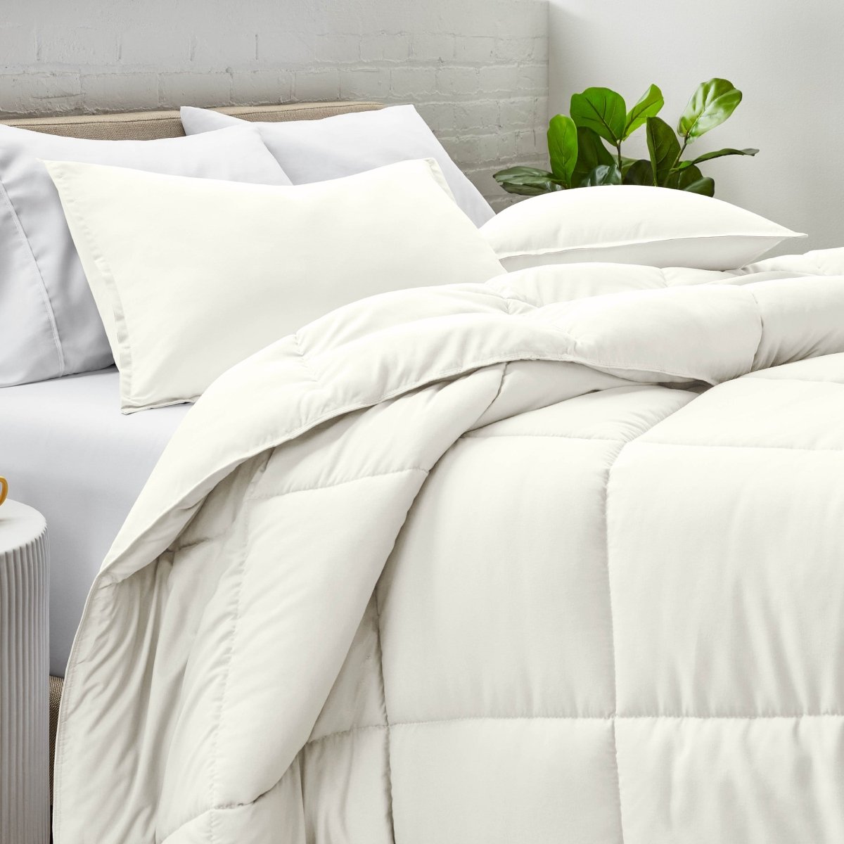 Comforter and pillow shams on a bed with a white brick wall and plant in the background