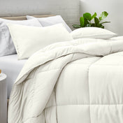 Comforter and pillow shams on a bed with a white brick wall and plant in the background
