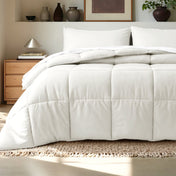 Comforter on a bed in a bedroom setting with a wooden nightstand and decorative items.