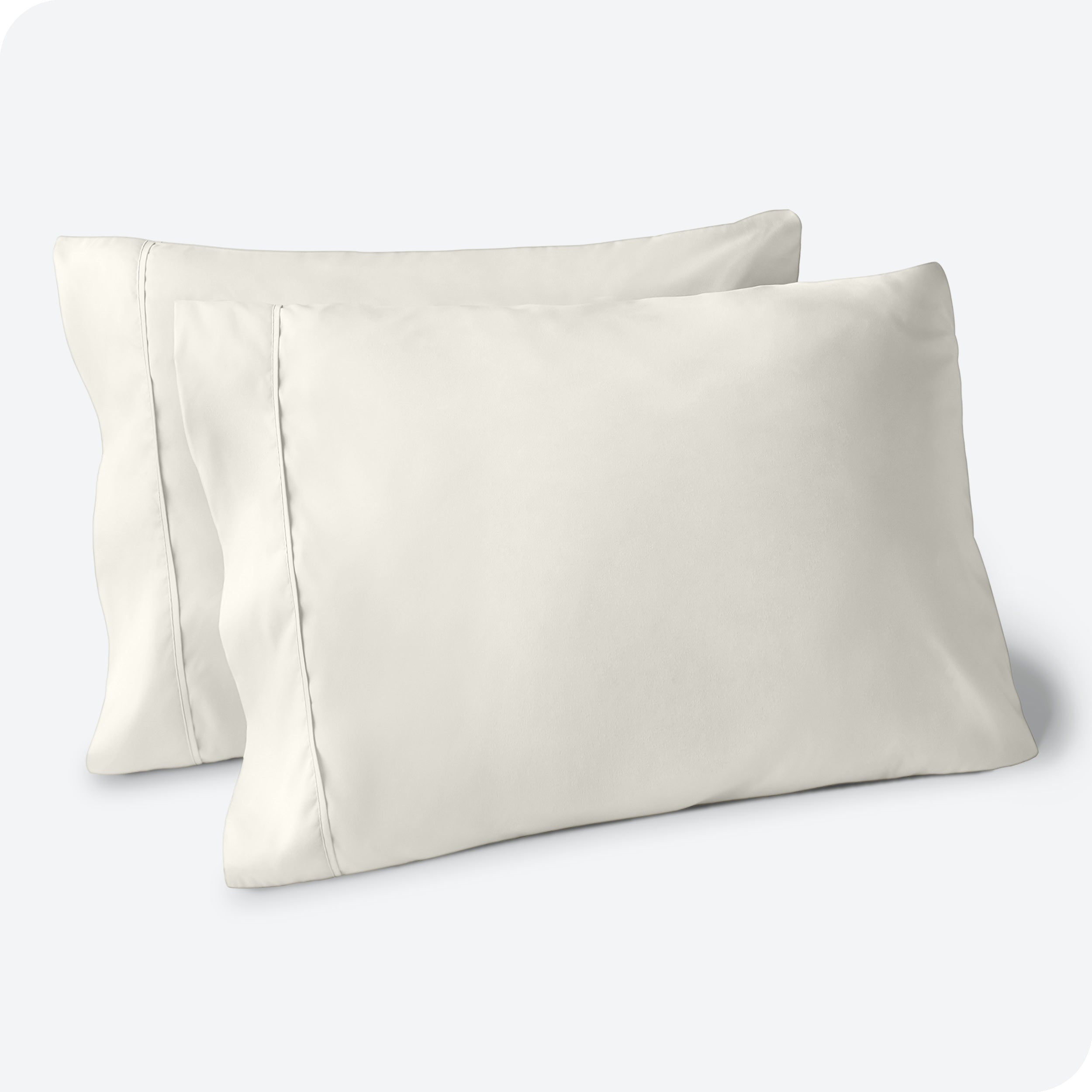 Two pillows on a white background with cream pillowcases on them