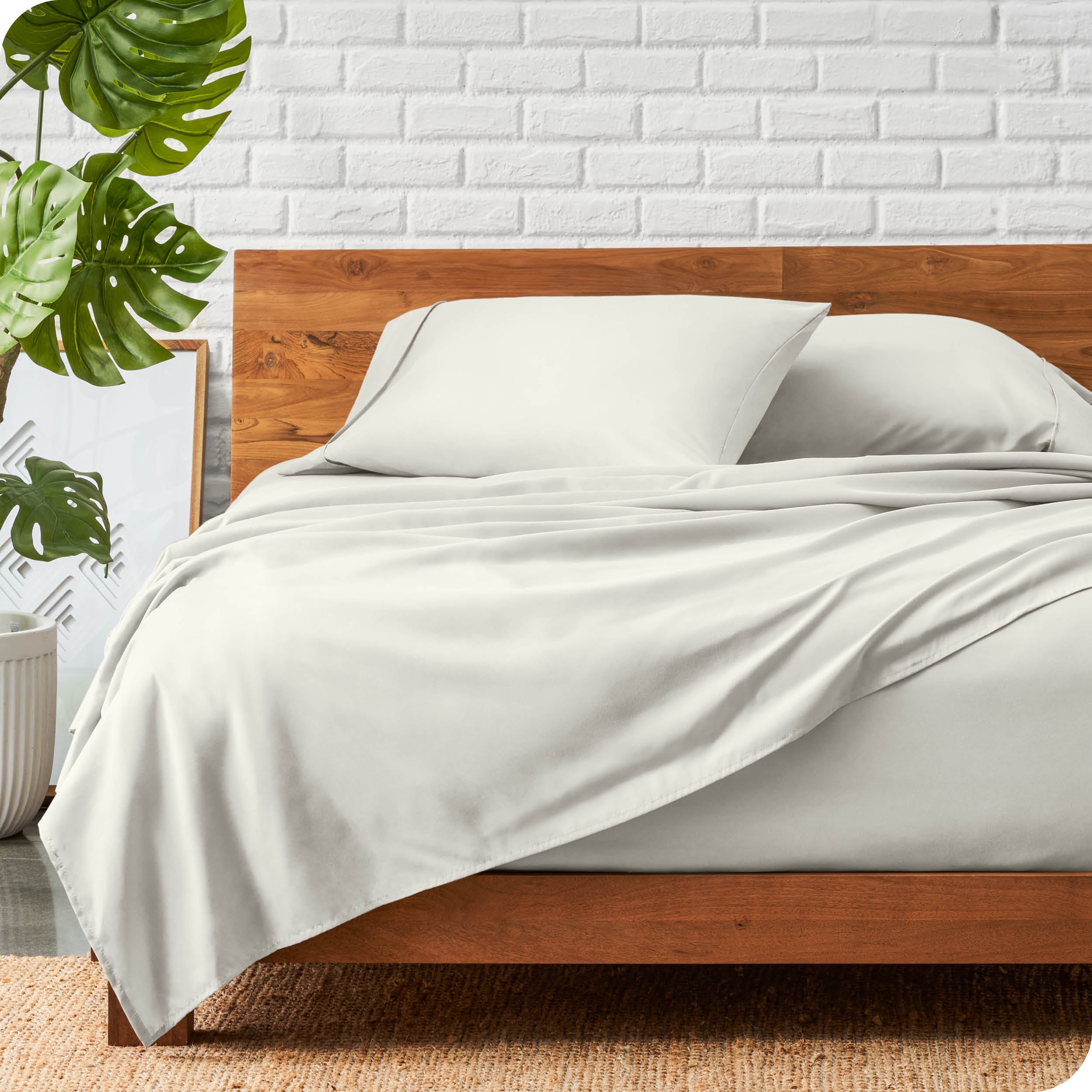 A wooden bed frame with a microfiber sheet set on the mattress.