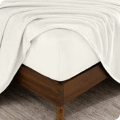 The corner of a bed frame and mattress with a fitted sheet and flat sheet on it.