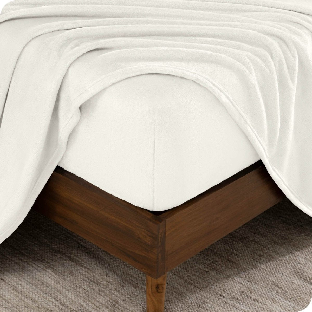 The corner of a bed frame and mattress with a fitted sheet and flat sheet on it.