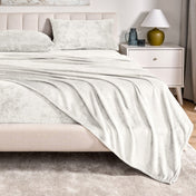 Microplush sheet set on a bed in a bedroom setting with a nightstand and lamp.