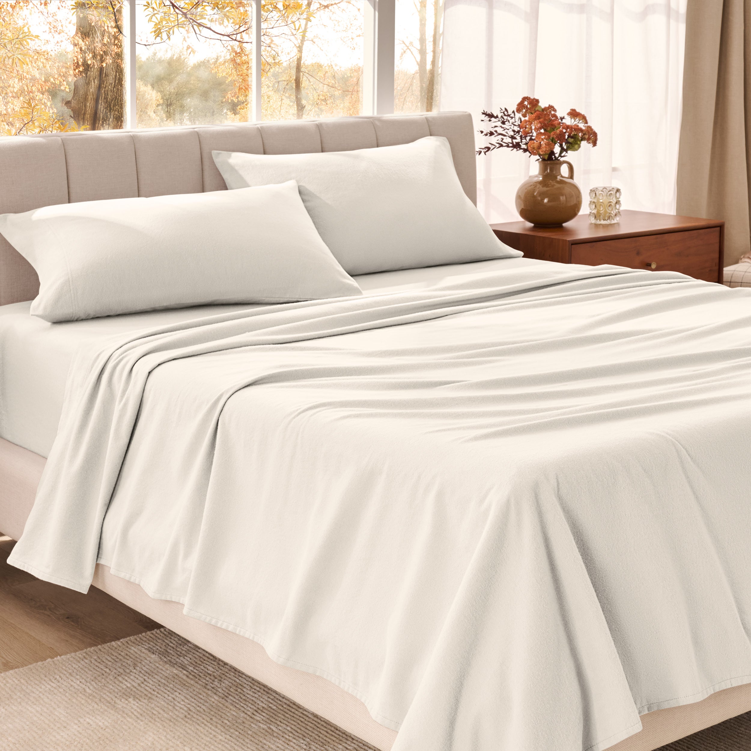 Bed sheets on a neatly made bed in a bright bedroom with large windows.