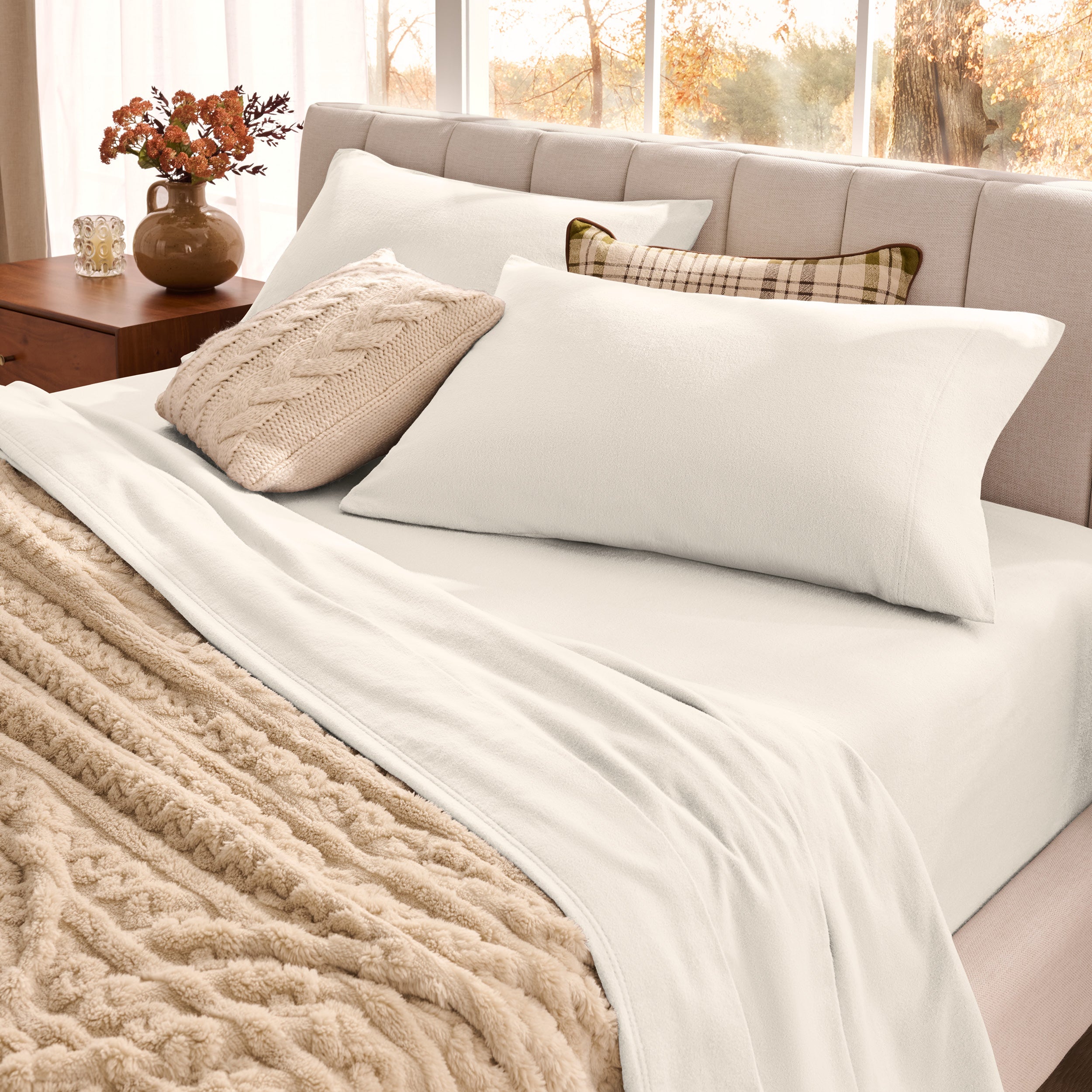 Neatly made bed with organic flannel sheets  and a beige blanket in a bright bedroom.