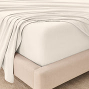 Fitted sheet and top sheet on a mattress with a beige bed frame