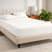 Fitted sheet on a bed in a bedroom setting with a lamp and plant.