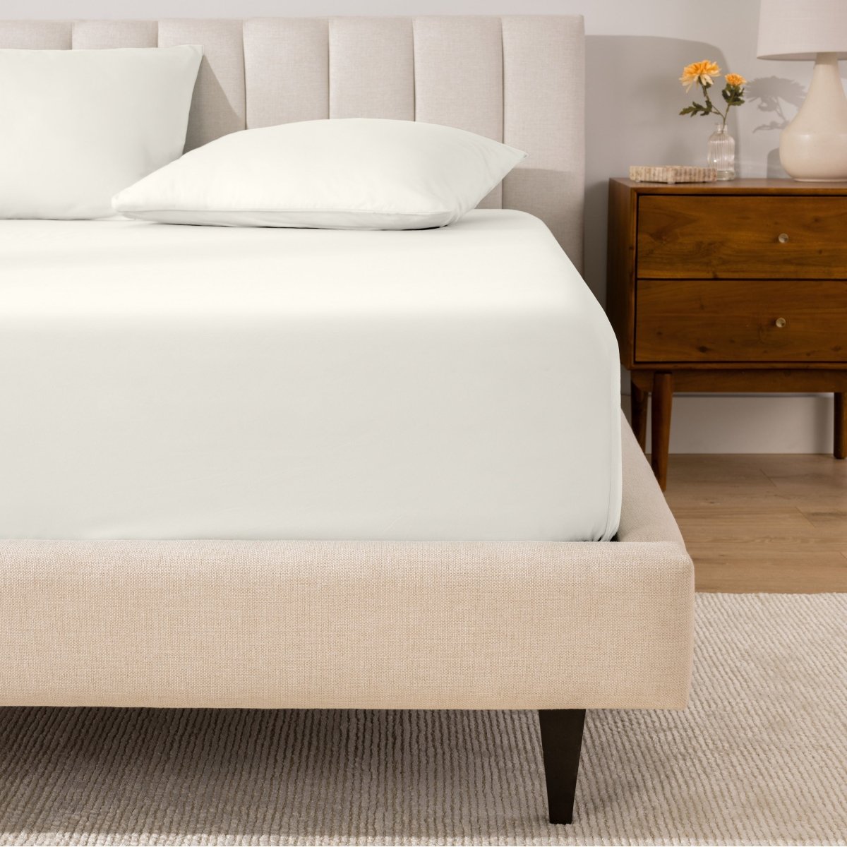 A percale fitted sheet and pillowcases on a bed in a bedroom with a wooden nightstand.