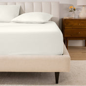 A percale fitted sheet and pillowcases on a bed in a bedroom with a wooden nightstand.