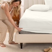 Woman in pajamas adjusting bed sheets on a bed.