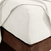 Corner of the bed with a fitted sheet on the mattress and a flat sheet draped over the side and end