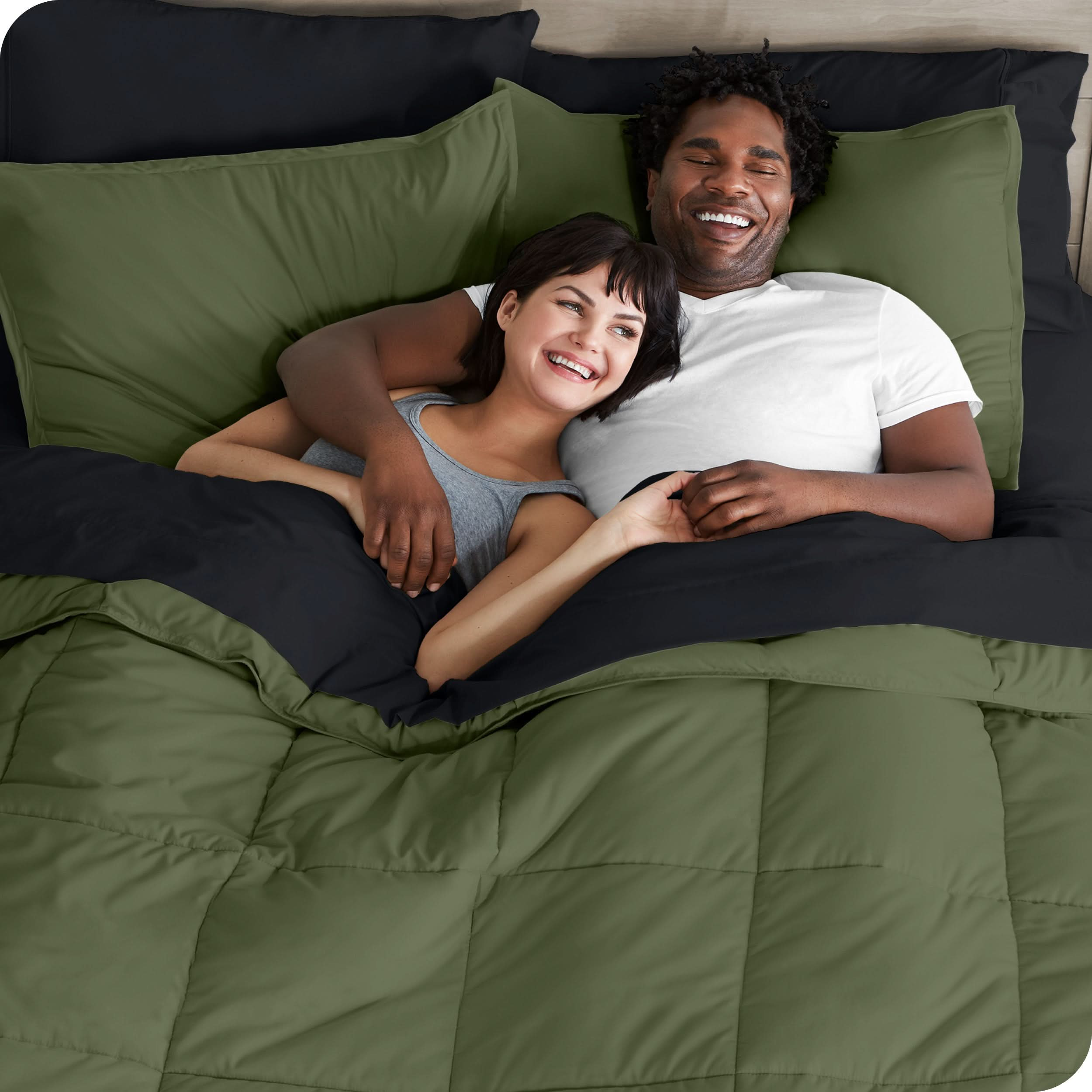 A couple is lying in bed with a comforter and sheets over them