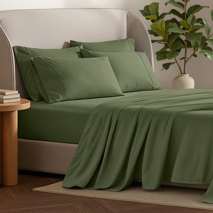 Bed sheets and pillows on a bed with a plant and side table in the background.