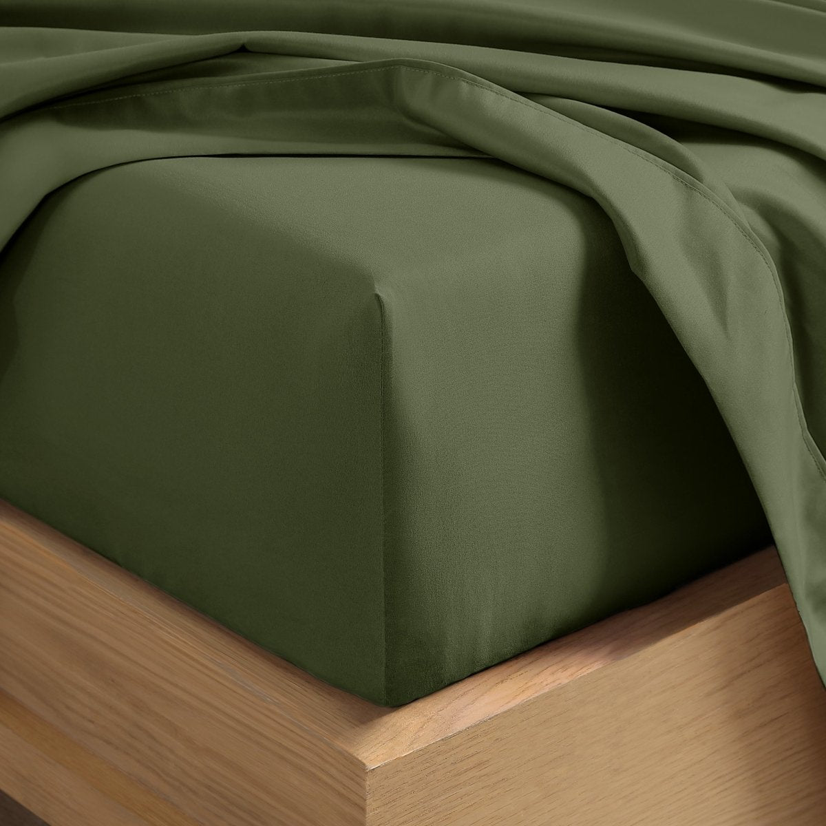 A close-up of a fitted sheet covering the corner of a bed frame, with matching top sheet draped over it.