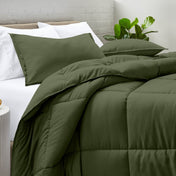 Comforter and pillow shams on a bed with a white brick wall and plant in the background