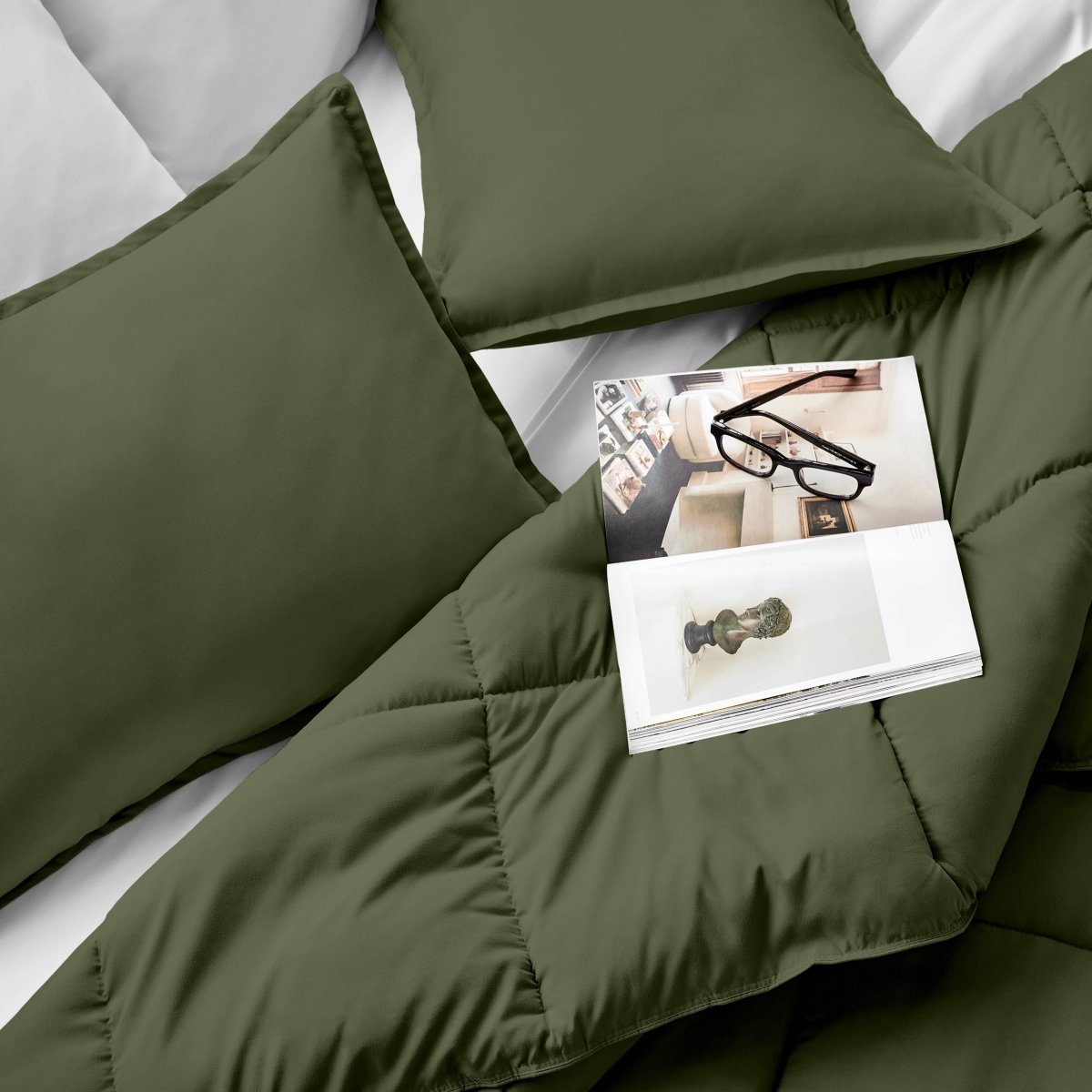 Comforter and pillows on a bed with a magazine and glasses.