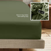 A fitted bed sheet on a bed frame with a small inset close-up of the elastic and a sewn-in tag labeled BOTTOM. White text on the sheet reads, 'Sewn-in tag makes bed-making easy.