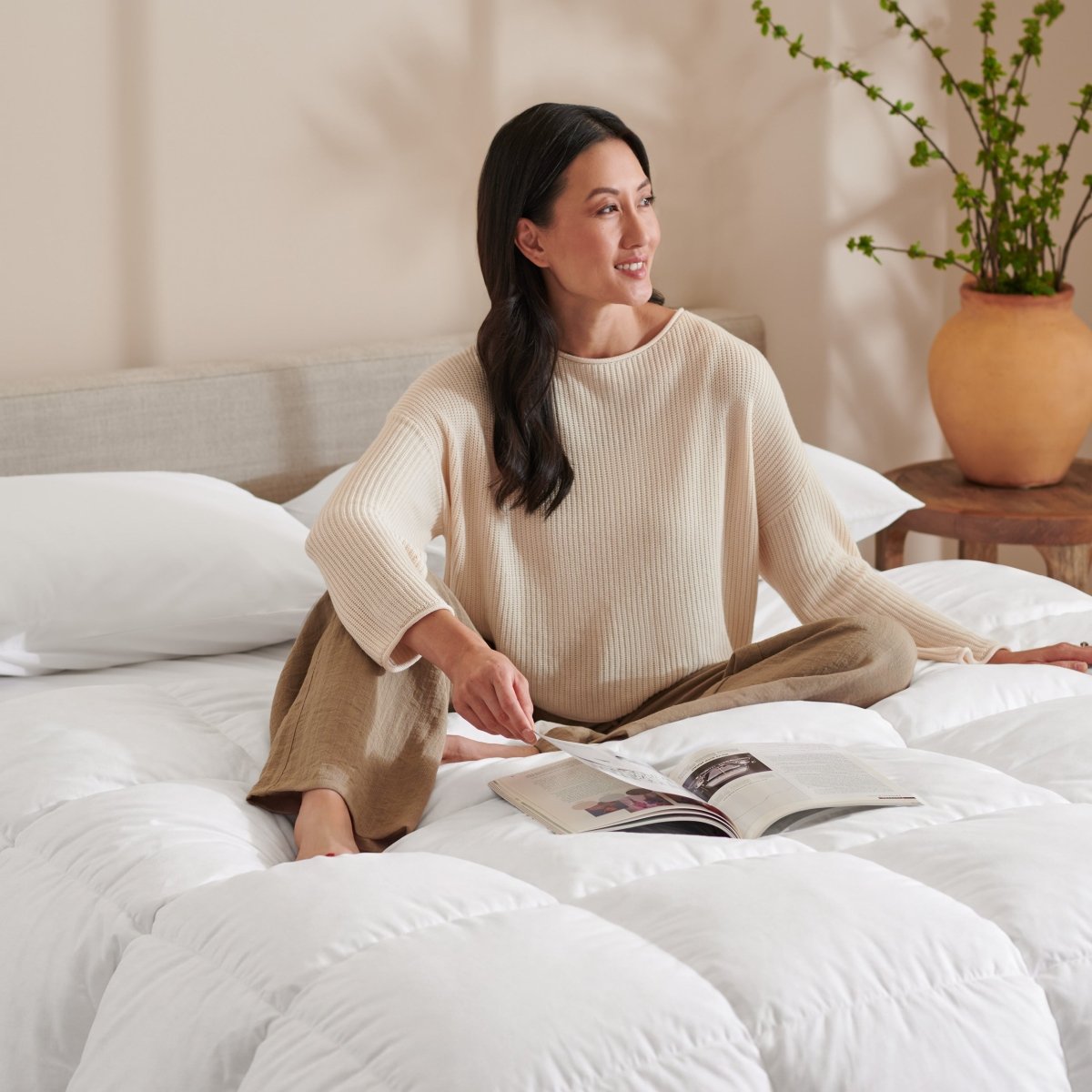 Woman reading a magazine on a bed with a neutral background