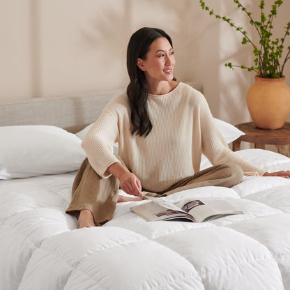 Woman reading a magazine on a bed with a neutral background