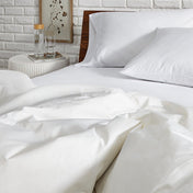 White bedding set on a bed with a nightstand in the background.