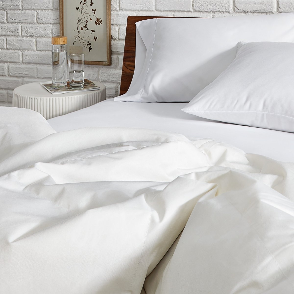 White bedding set on a bed with a nightstand in the background.