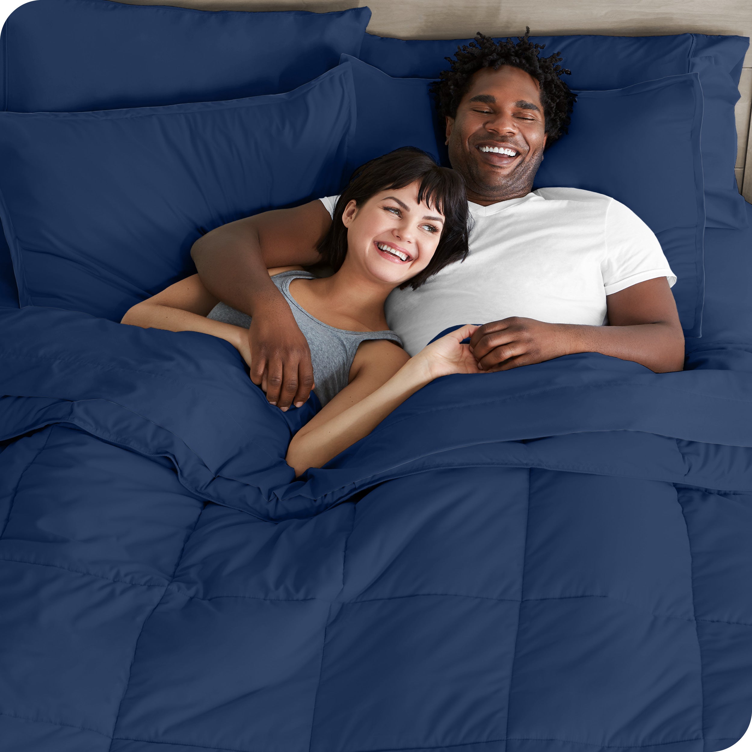 A couple is lying in bed with a comforter and sheets over them