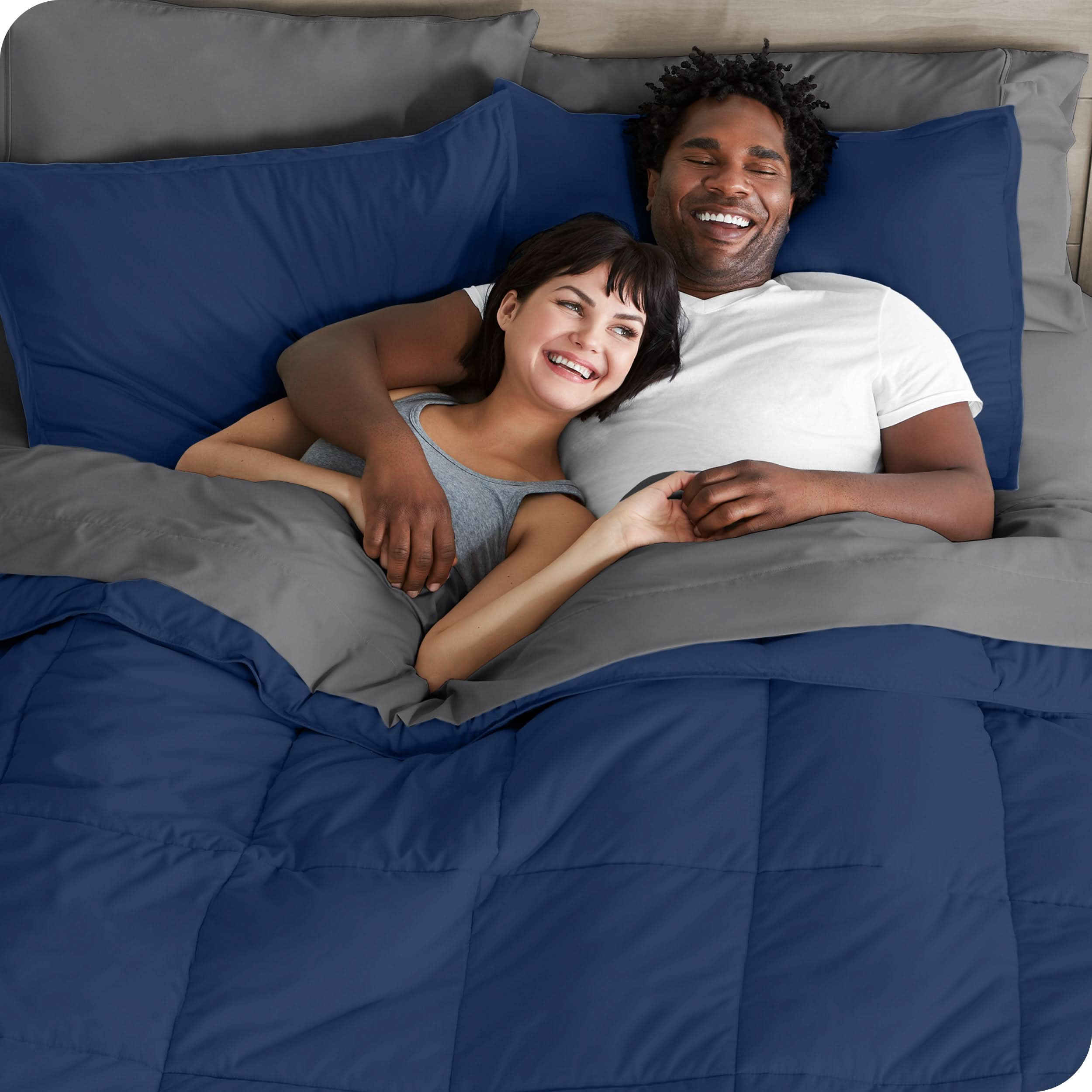 A couple is lying in bed with a comforter and sheets over them