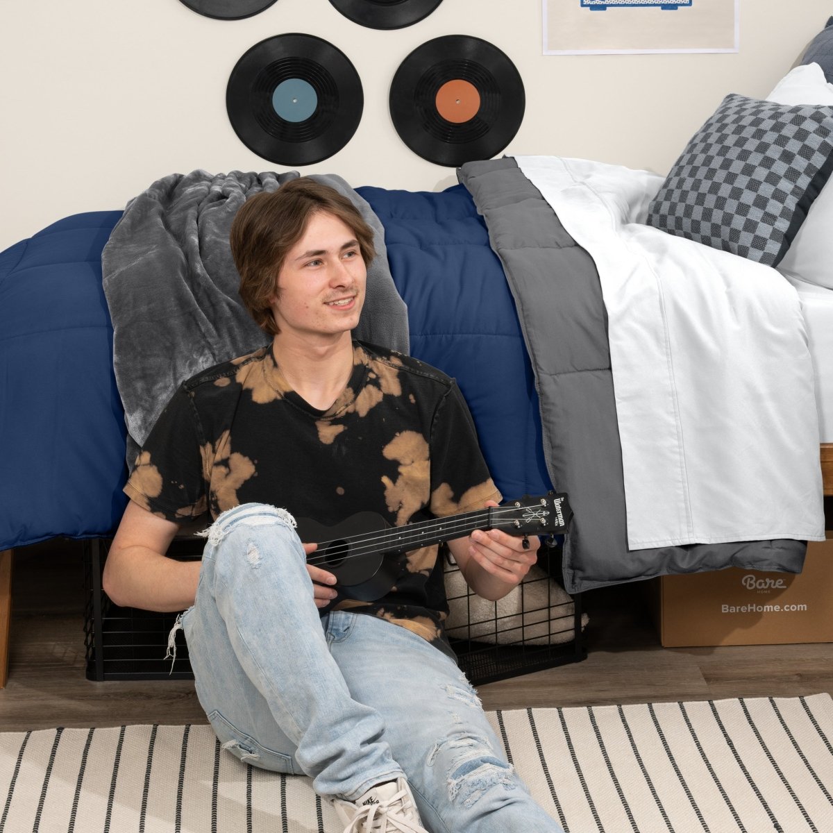 Person sitting on a bed holding a guitar in a bedroom setting with vinyl records on the wall.