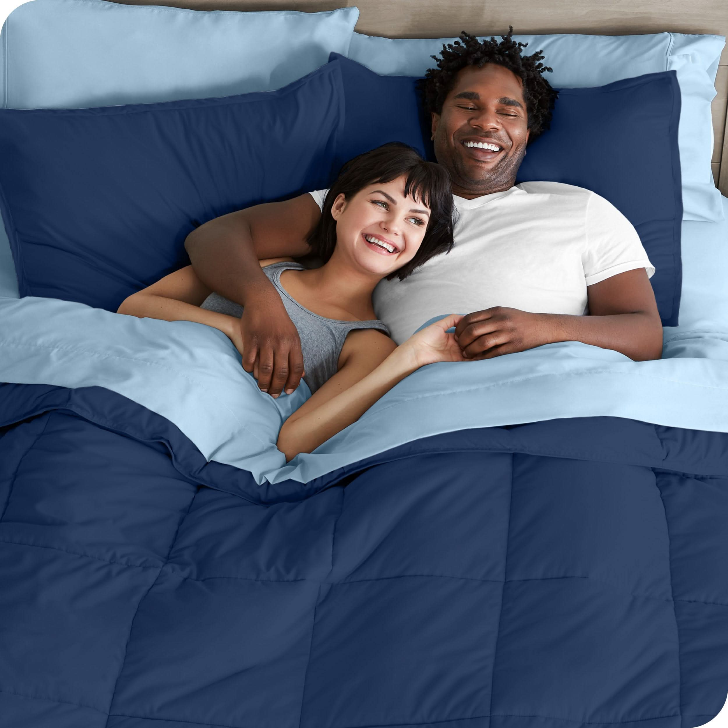 A couple is lying in bed with a comforter and sheets over them