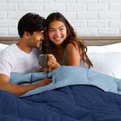Man and woman sitting on a bed holding a mug, smiling at each other.