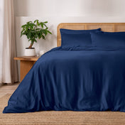 Dark blue bedding set on a bed with a wicker headboard and side table with a plant.