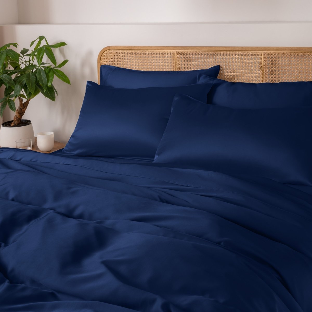 Dark blue bedding set on a bed with a wicker headboard and plant in the background.
