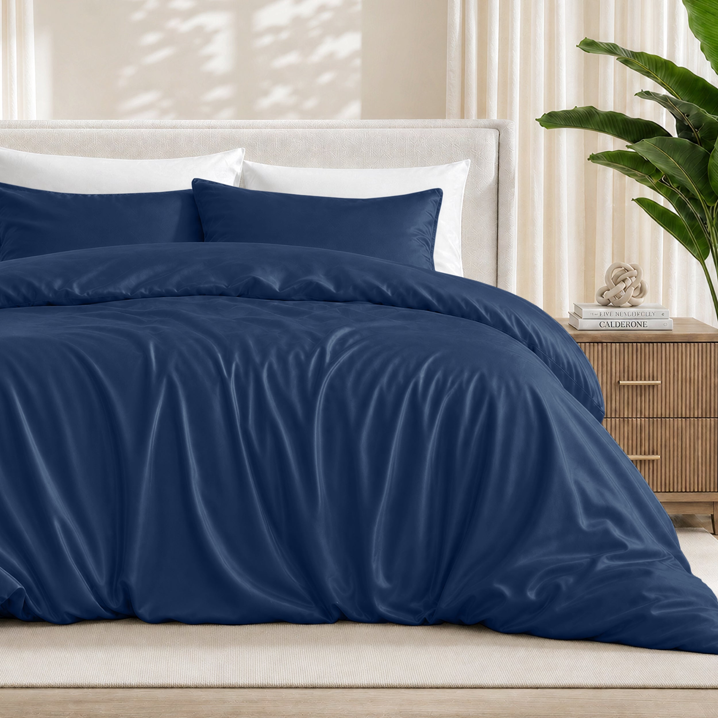 Dark blue duvet cover set on a bed in a bedroom setting with a plant and nightstand.