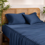 Bamboo bed sheets and pillows on a bed with a wicker headboard in a room with plants.