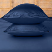 Two blue pillows stacked on a bed with a woven headboard.