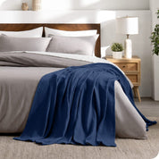 A cotton waffle blanket is on the corner of a bed. It is hanging down the side and end of the bed.